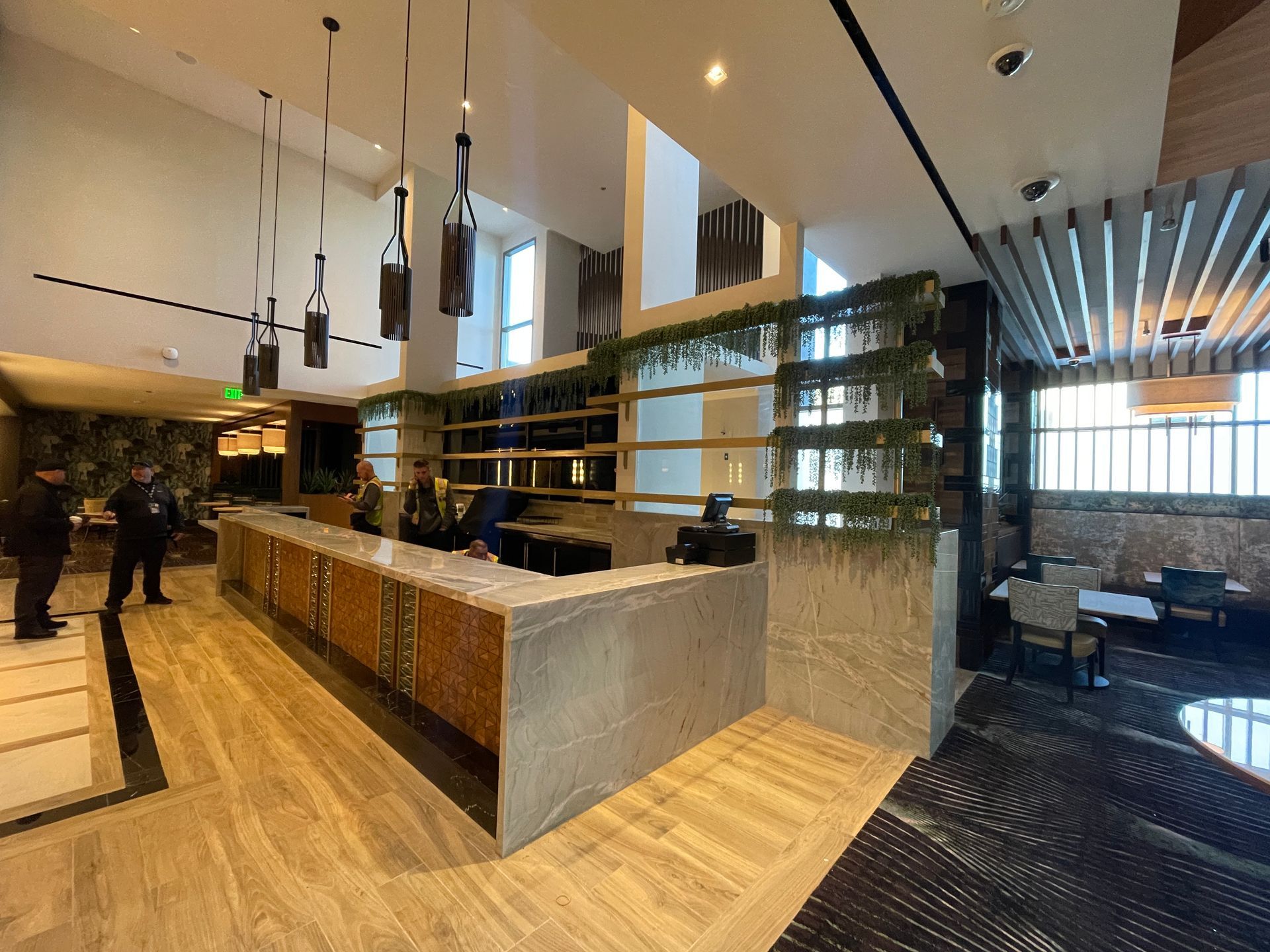 Modern hotel lobby with wood reception desk, seating, tall windows, and green plant wall