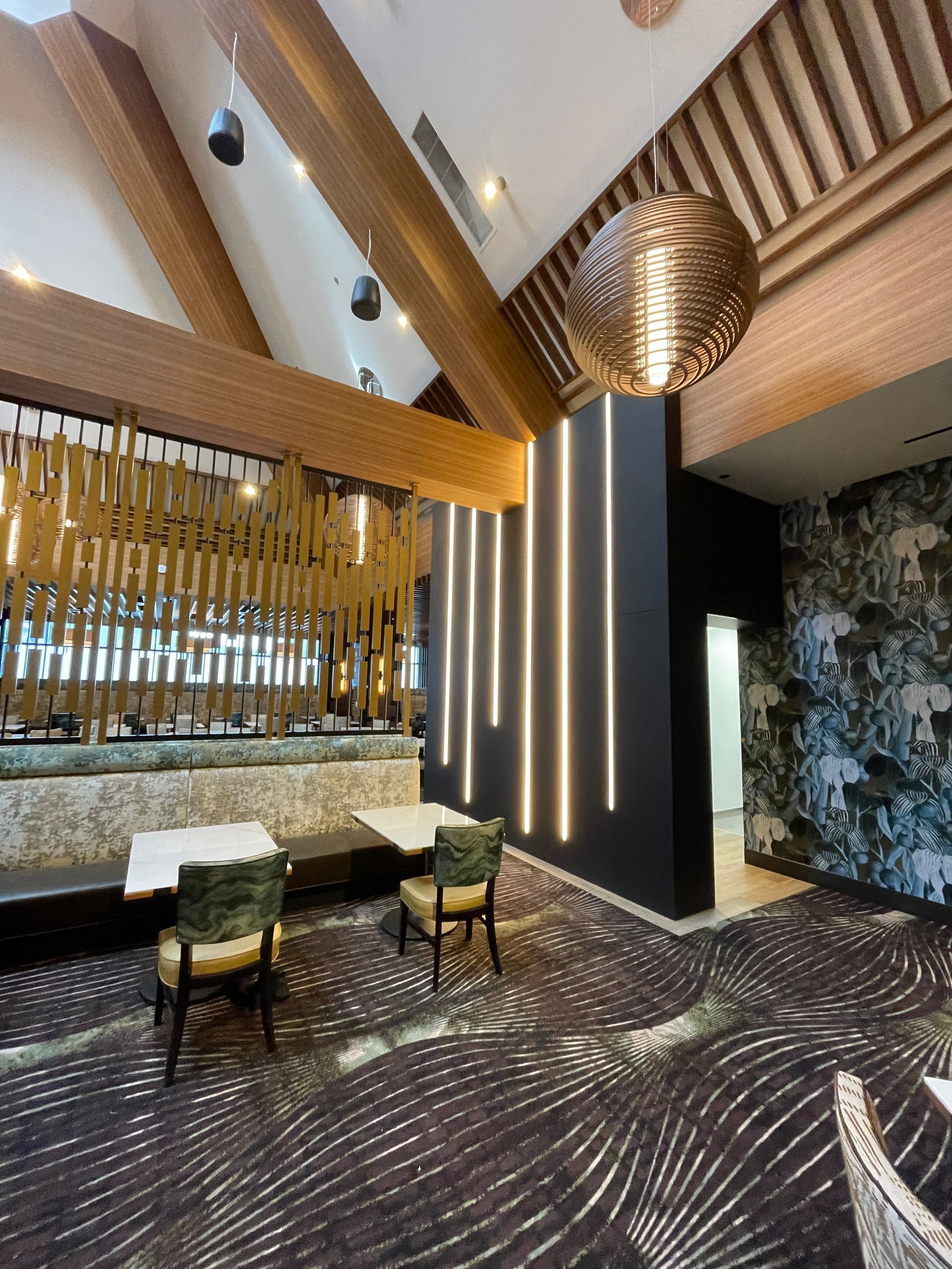 Stylish modern lounge with patterned carpet, tall wood ceiling, hanging pendant light, and cushioned chairs