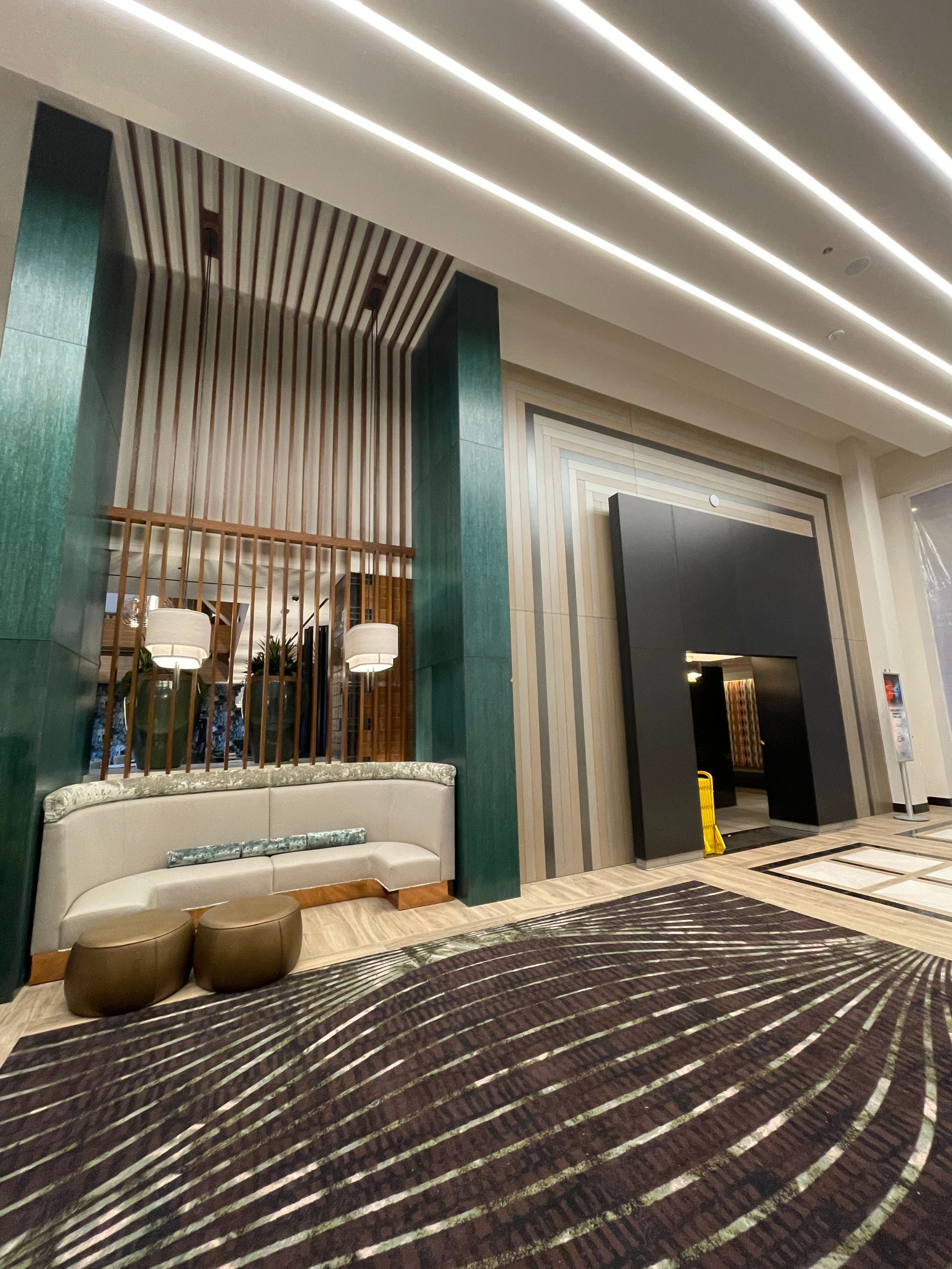 Modern hotel lobby with teal columns, curved sofa, and patterned carpet under bright ceiling lights