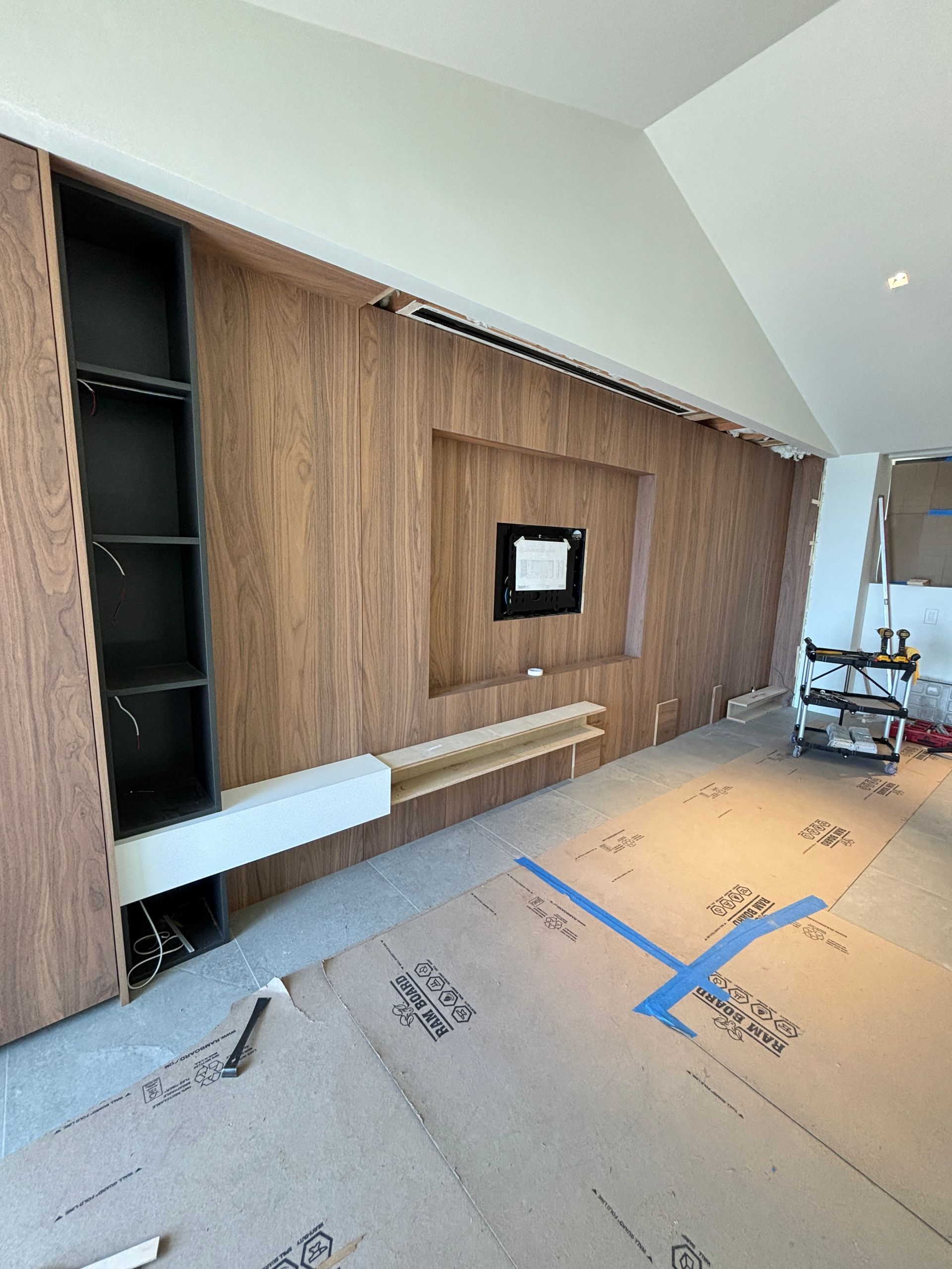 Modern living room wall with wood paneling, built-in shelving, a TV mount, and cardboard floor protection during renovation