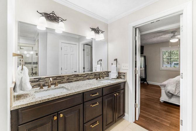 Bathroom remodel showing vanity with granite countertop, dark cabinets, and mirror; bedroom visible through open doorway