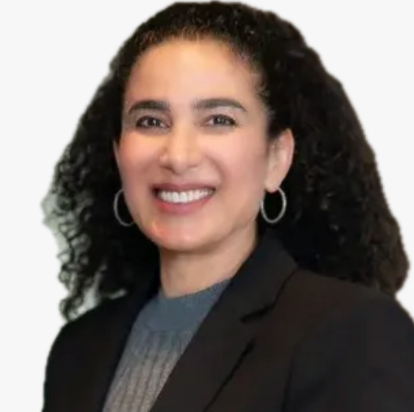 Woman with curly hair smiles, wearing a black blazer and hoop earrings.