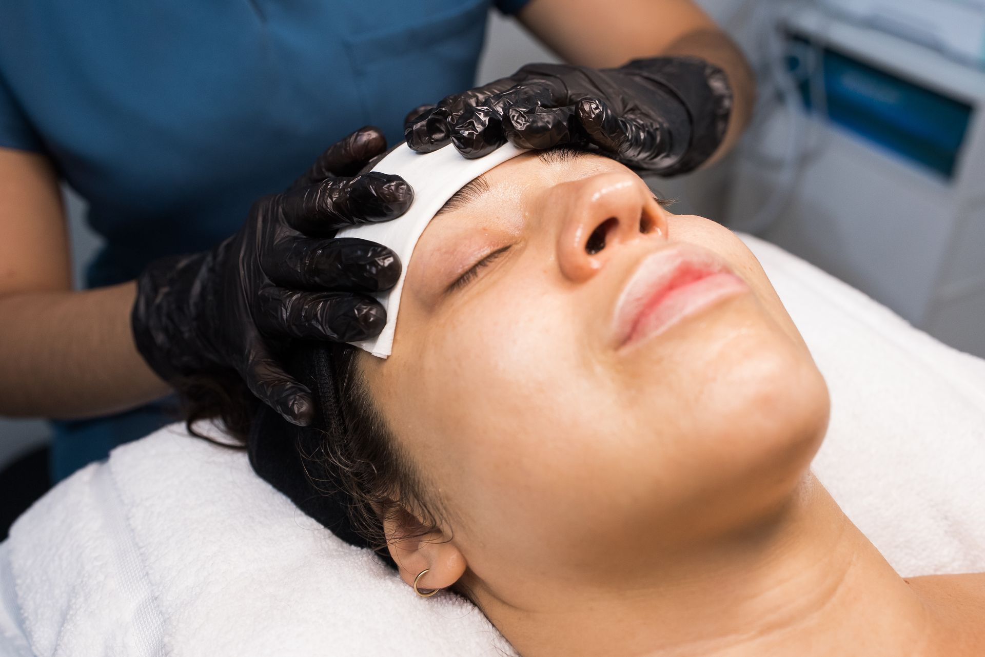 Close-up of cosmetologist performing facial peeling treatment on woman.