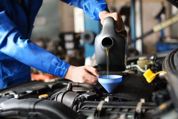 Mechanic pouring oil into a car engine through a funnel in a repair shop