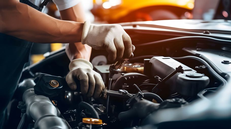 Mechanic wearing gloves working under a car hood in a garage