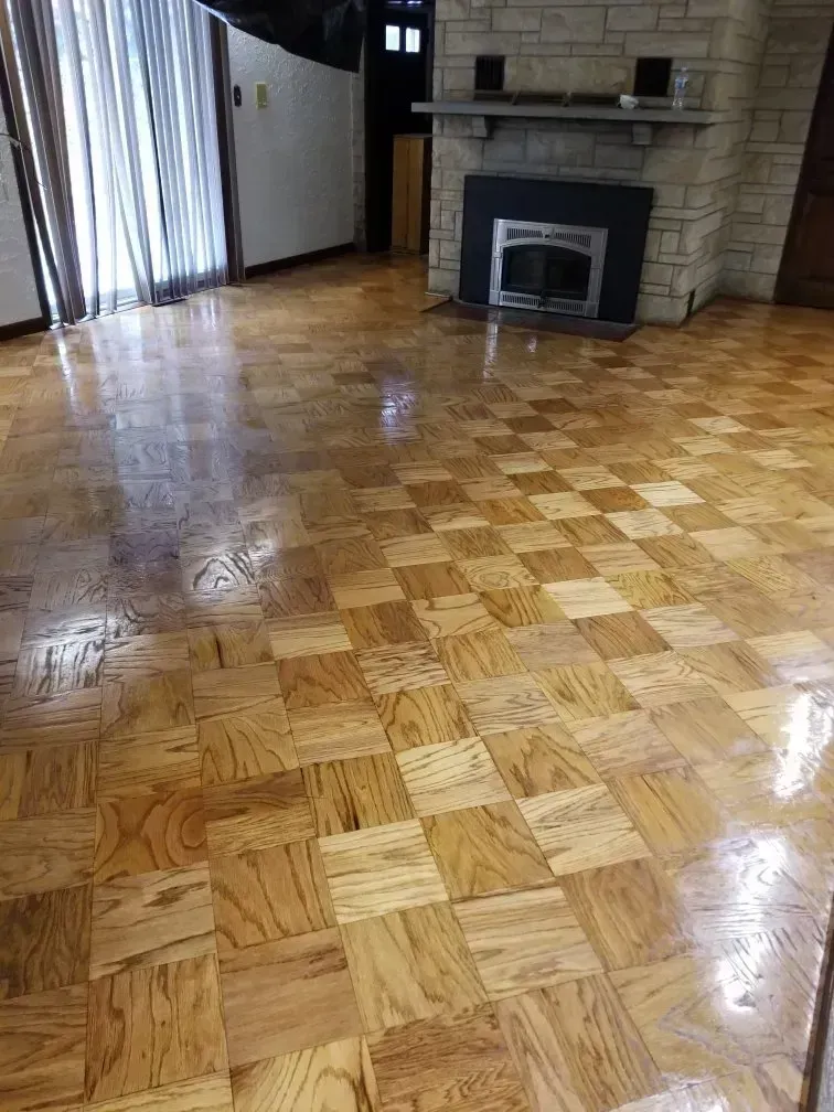 Wooden checkerboard-patterned floor in a room with a fireplace, curtains, and a dark doorway.