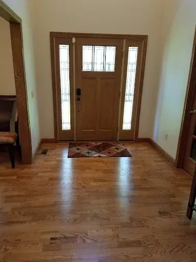 Wooden entryway with door, sidelights, and hardwood floors. A rug sits in front of the door.