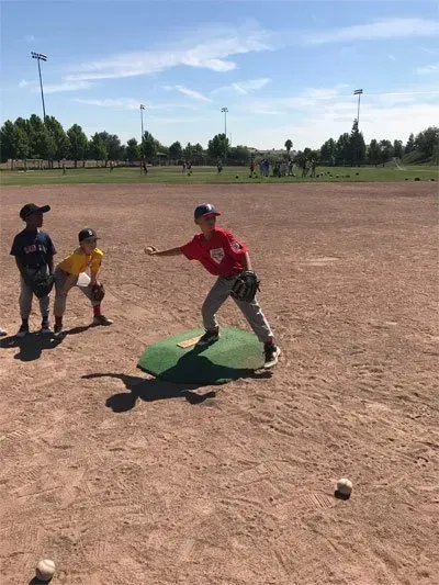 Children playing baseball on a dusty field, with one swinging at the ball and two waiting nearby.