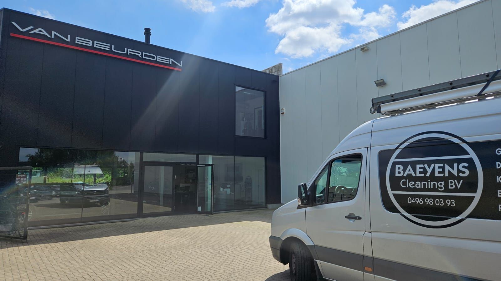 Een wit busje staat geparkeerd voor een gebouw.