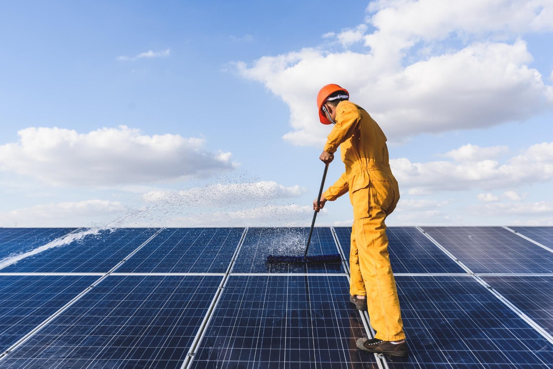 Een man maakt zonnepanelen schoon met een bezem.