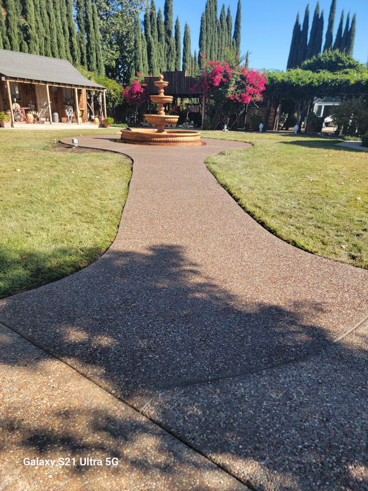 A concrete walkway leading to a fountain in front of a house
