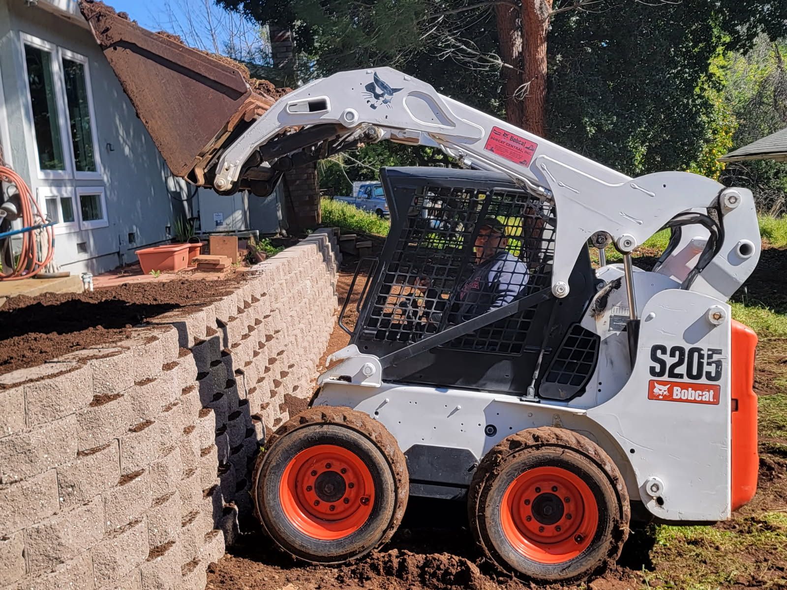A bobcat s205 is loading dirt into a bucket in front of a house