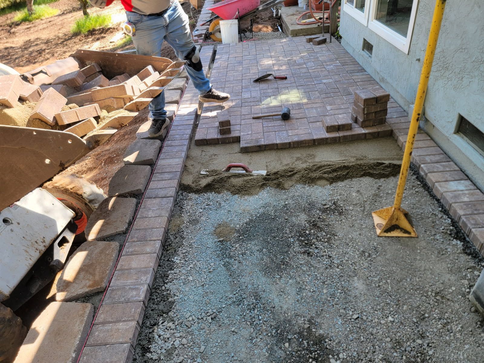 A man is laying bricks on a sidewalk in front of a house