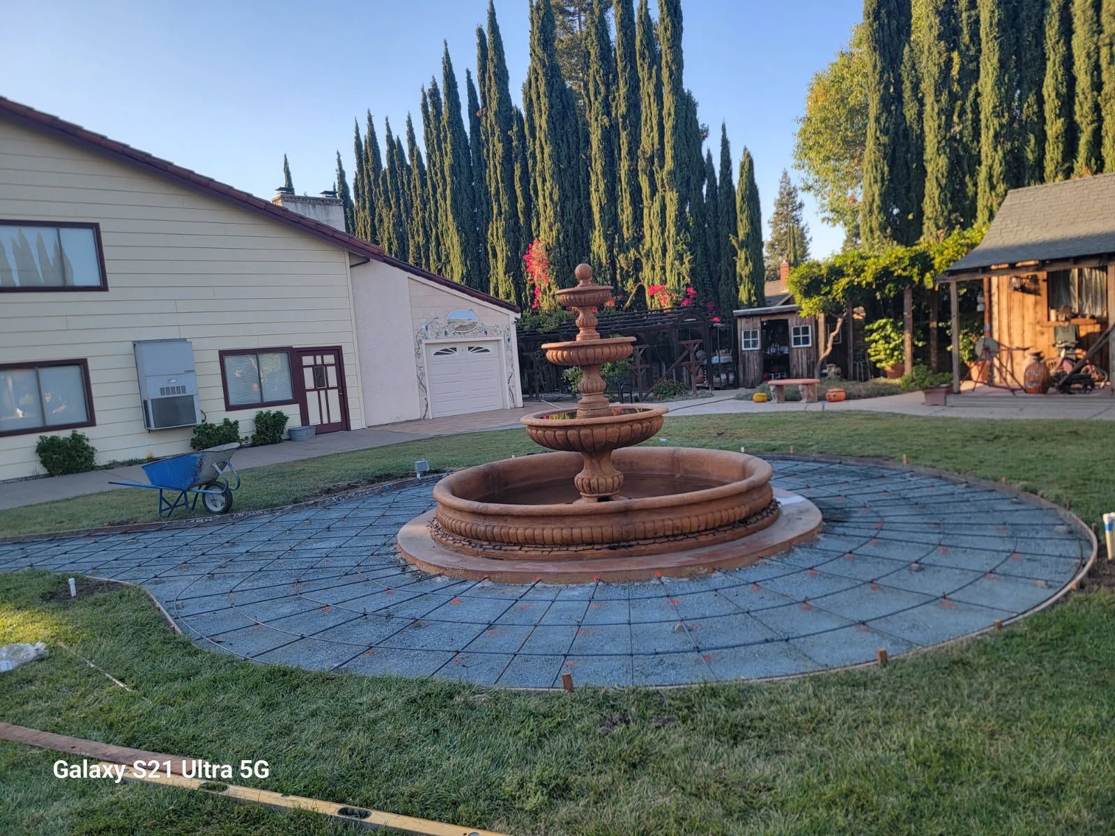 A large fountain is in the middle of a lush green yard in front of a house