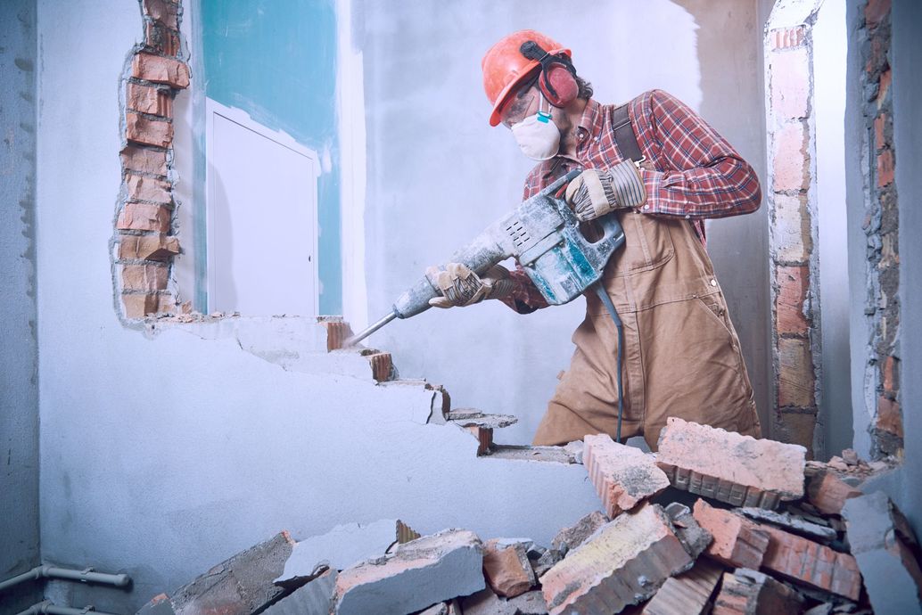 A Man is Using a Hammer to Demolish a Brick Wall