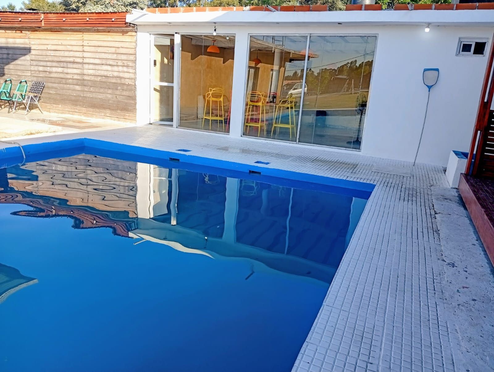Piscina en el patio trasero junto a una casa blanca con puertas correderas de cristal y reflejos azules en el agua