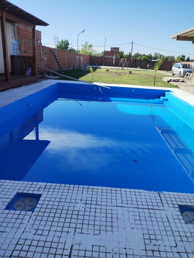 Piscina en el jardín trasero con agua azul brillante y una terraza de baldosas en un día soleado