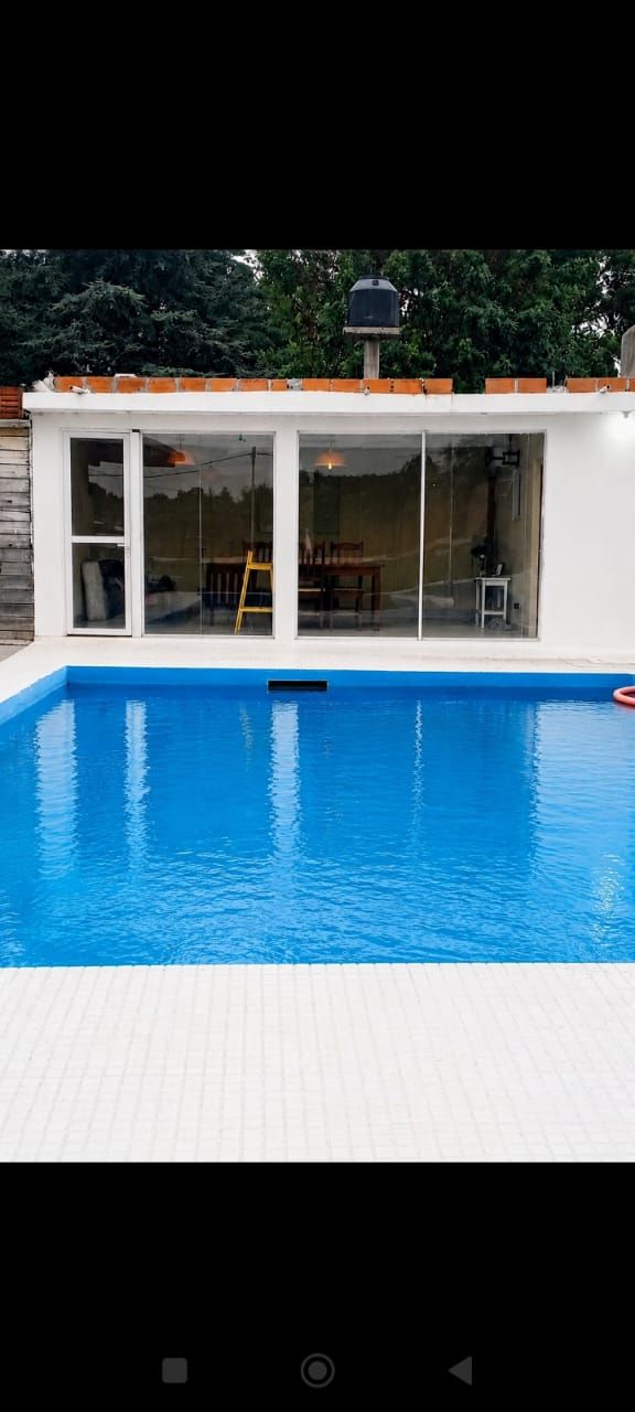 Piscina azul delante de una casa blanca con puertas de cristal y un tejado de tejas naranjas.