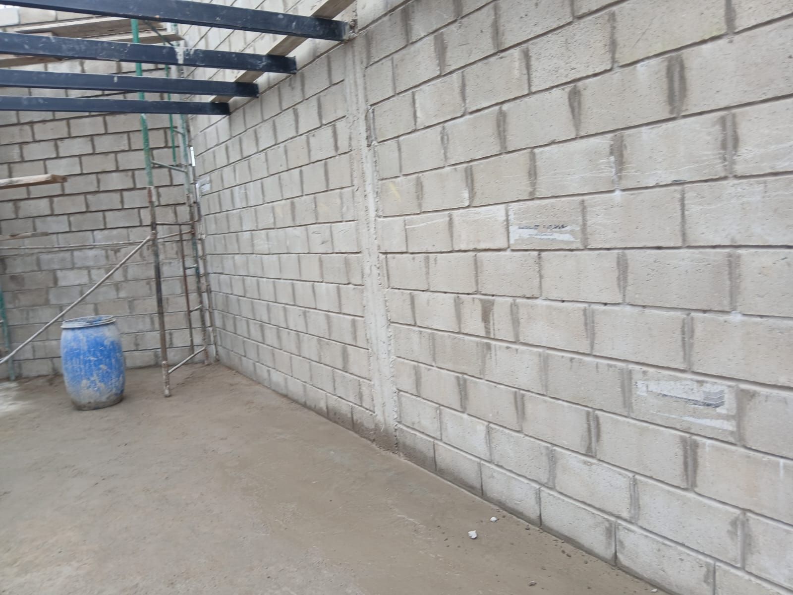 Habitación vacía de bloques de hormigón, con vigas del techo a la vista y un barril azul en una esquina
