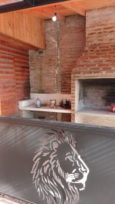 Cocina exterior de ladrillo con techo de madera, encimera con fregadero y parrilla empotrada bajo un tejado inclinado.
