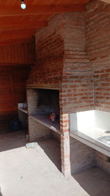 Barbacoa de ladrillo bajo un tejado de madera, con una encimera de hormigón y una zona de estar al aire libre.