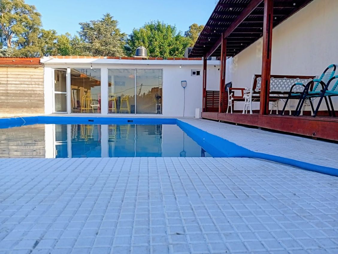 Piscina al aire libre junto a un patio con sillas y una casa moderna al fondo