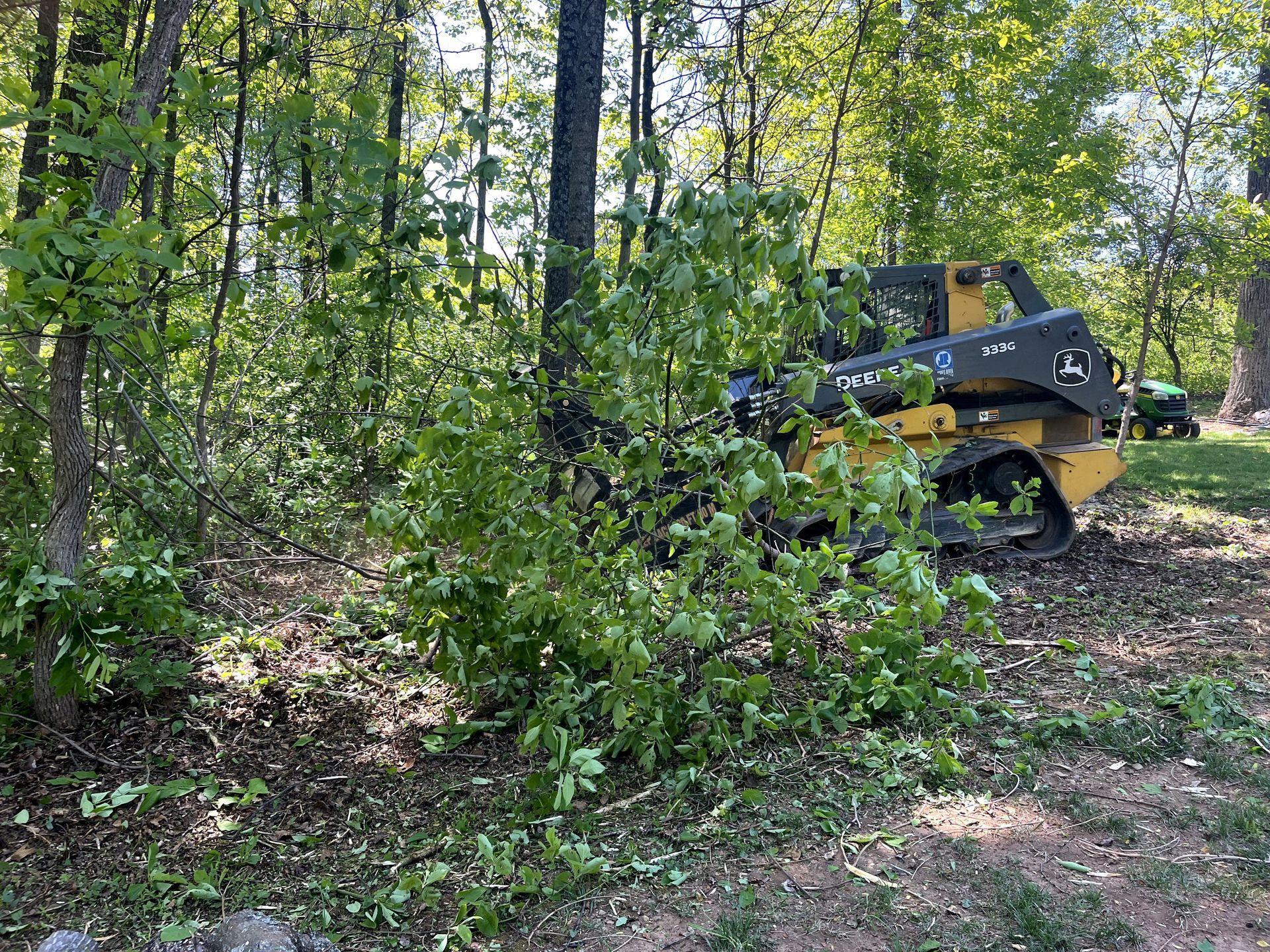 Yellow skid steer in a wooded area with a person working nearby