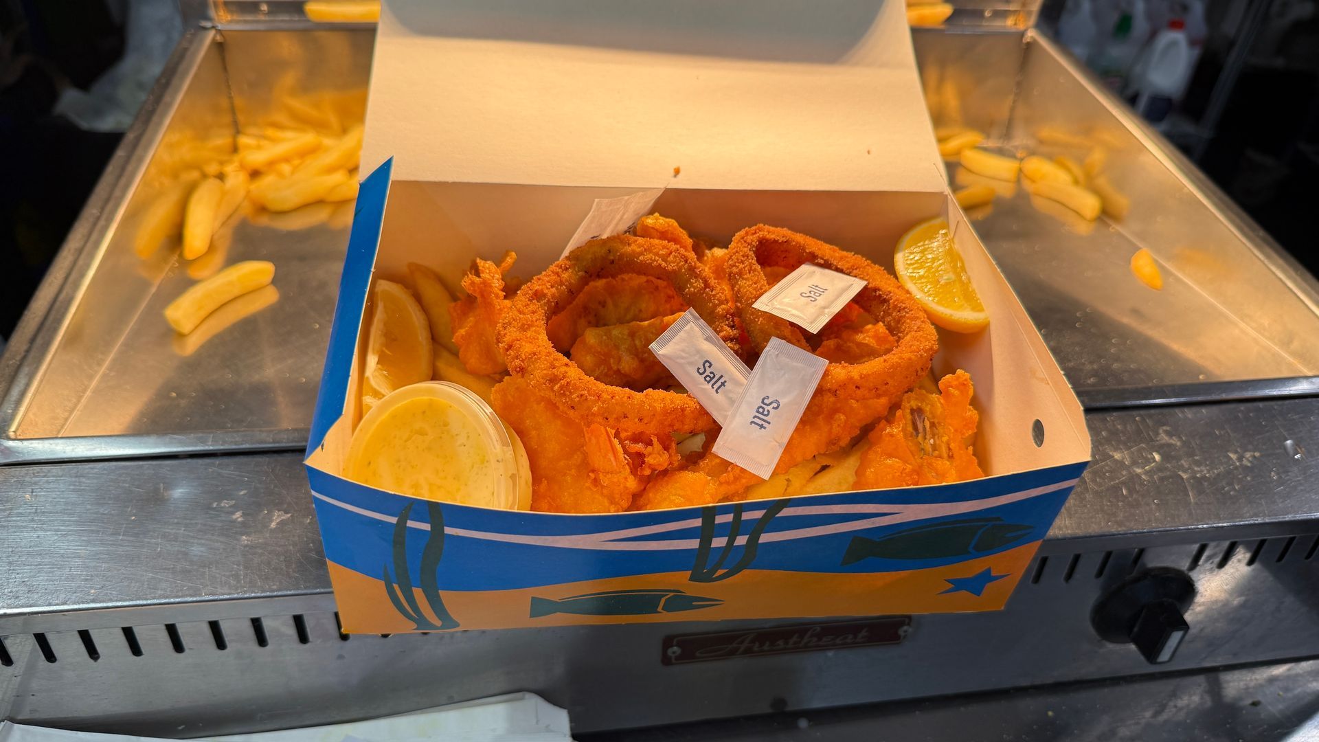 Fried food in a box with lemon slices and sauce packets; a fish and chips meal.
