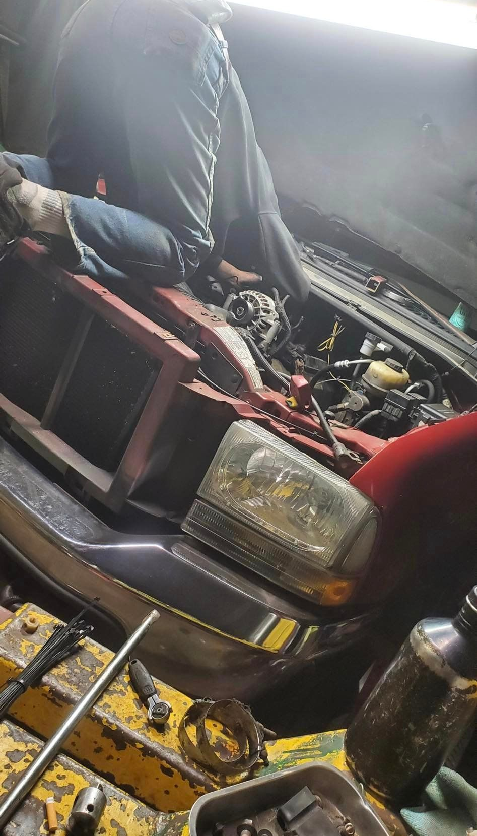 A person working on a red car with the hood open. Various tools and parts are visible.