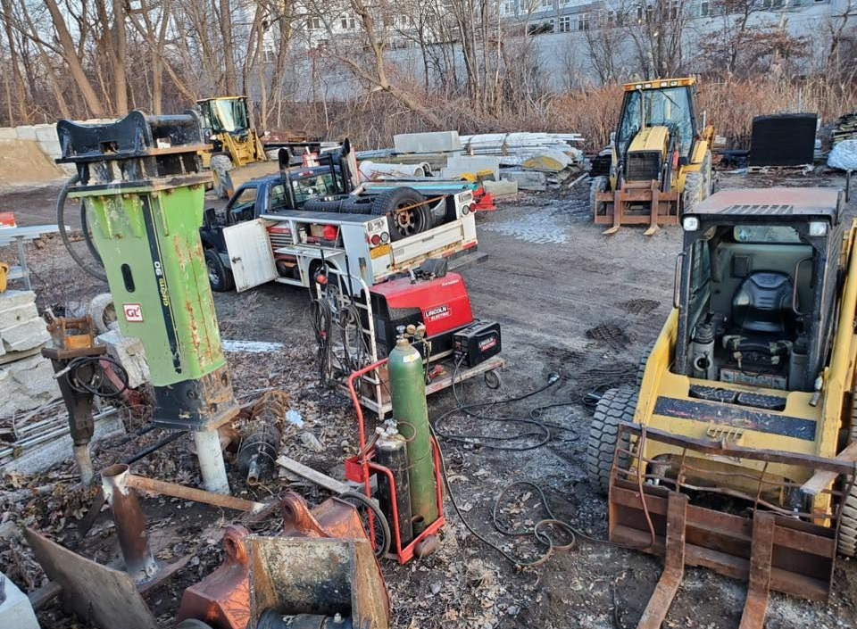 Construction equipment, including a skid steer and truck, sit in a lot. Welding equipment is present.