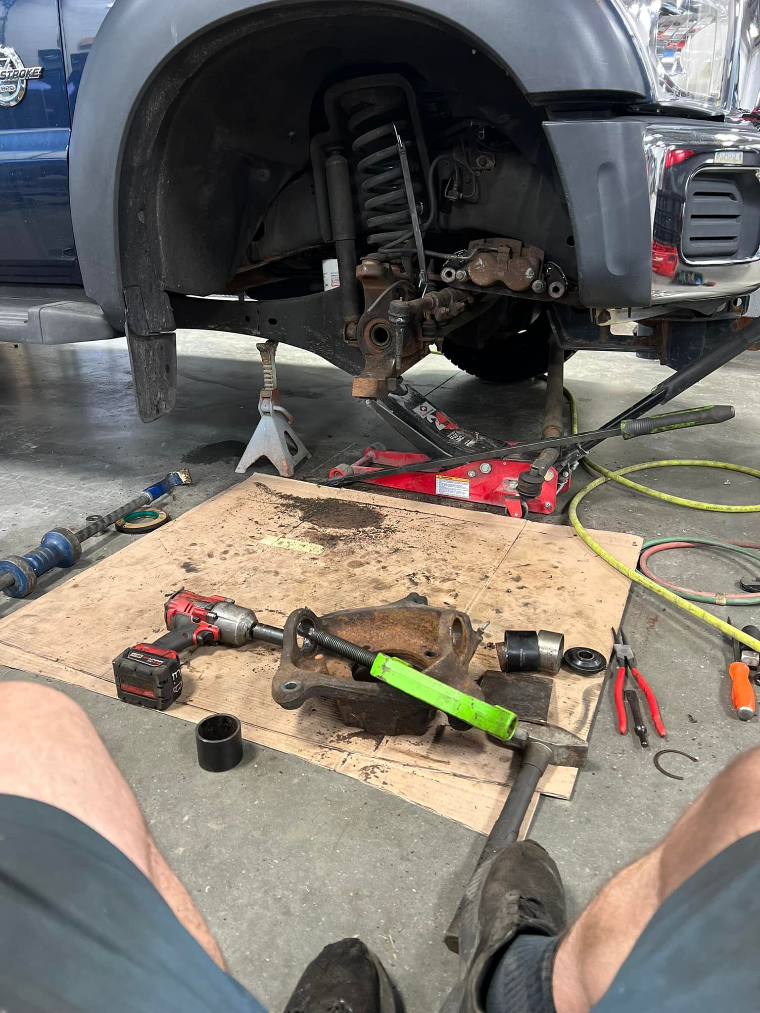 Truck suspension repair in progress; tools and parts on ground, truck raised on jack.