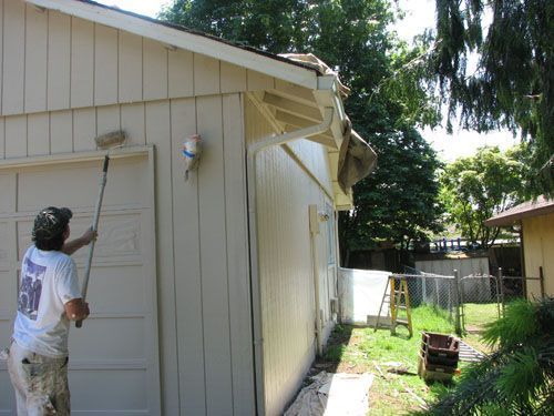 A man is painting the side of a house with a roller.