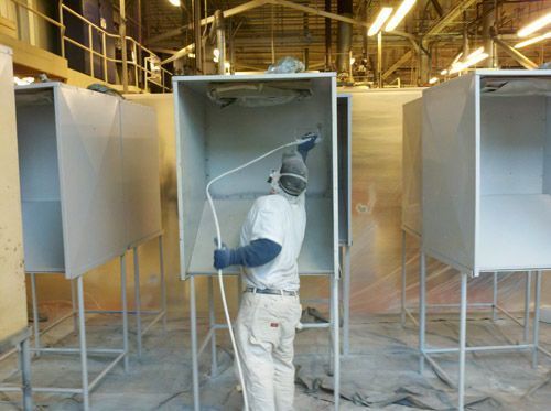 A man is spray painting a box in a factory.