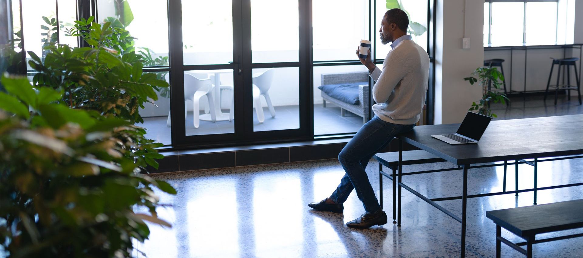 A man is sitting on a table in a room holding a cup of coffee.
