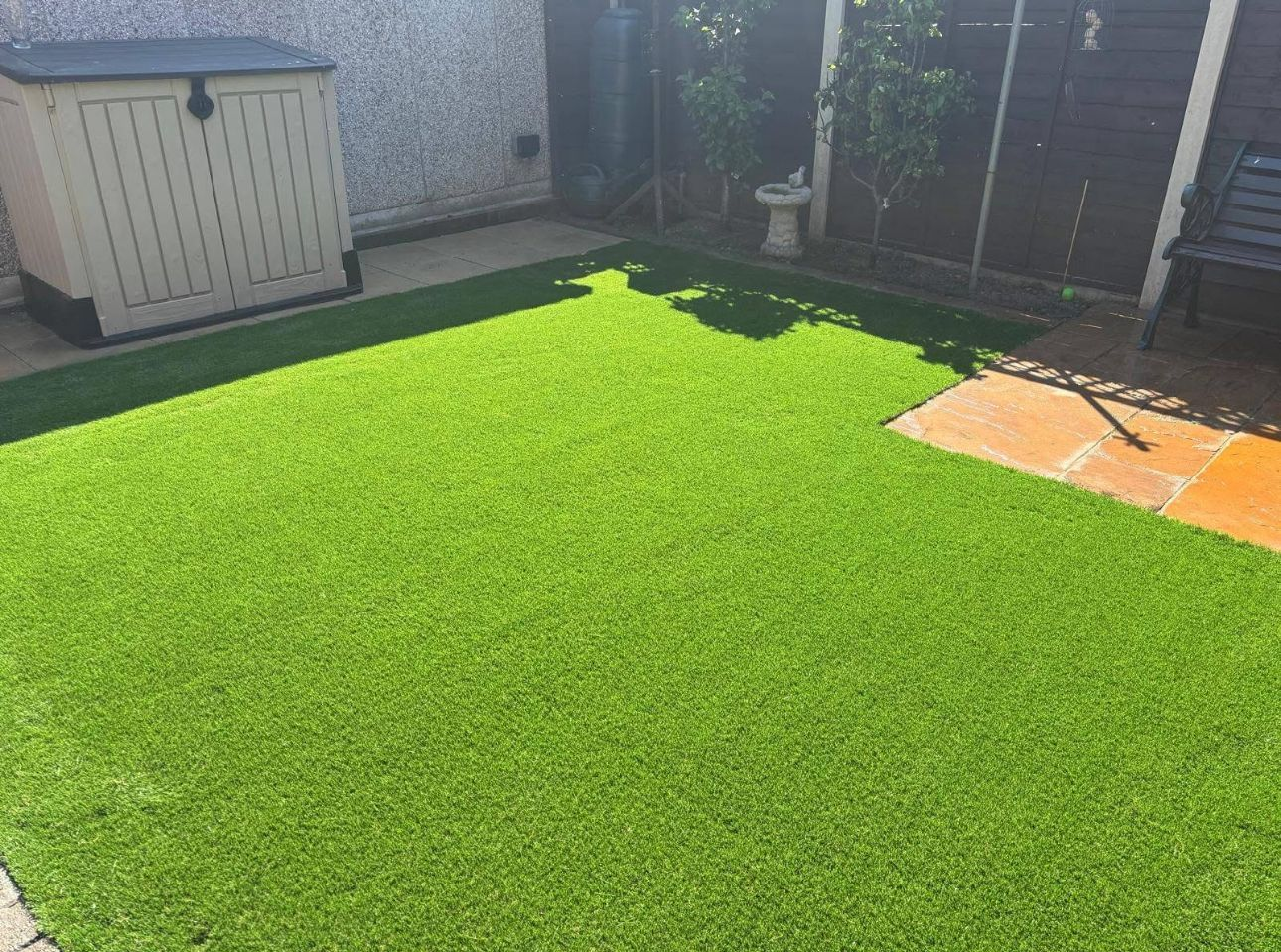 Backyard with bright artificial grass, storage shed, and patio stones in sunlight