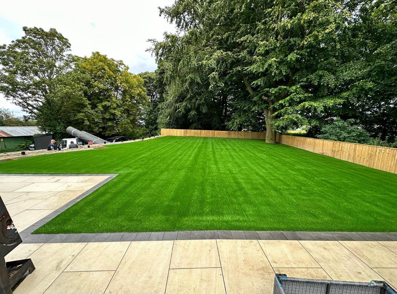 Bright green landscaped lawn with trees, patio stones, and a wooden fence in a backyard garden.