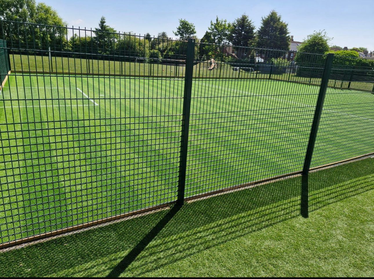 Black metal fence along a green grassy field in a sunny park