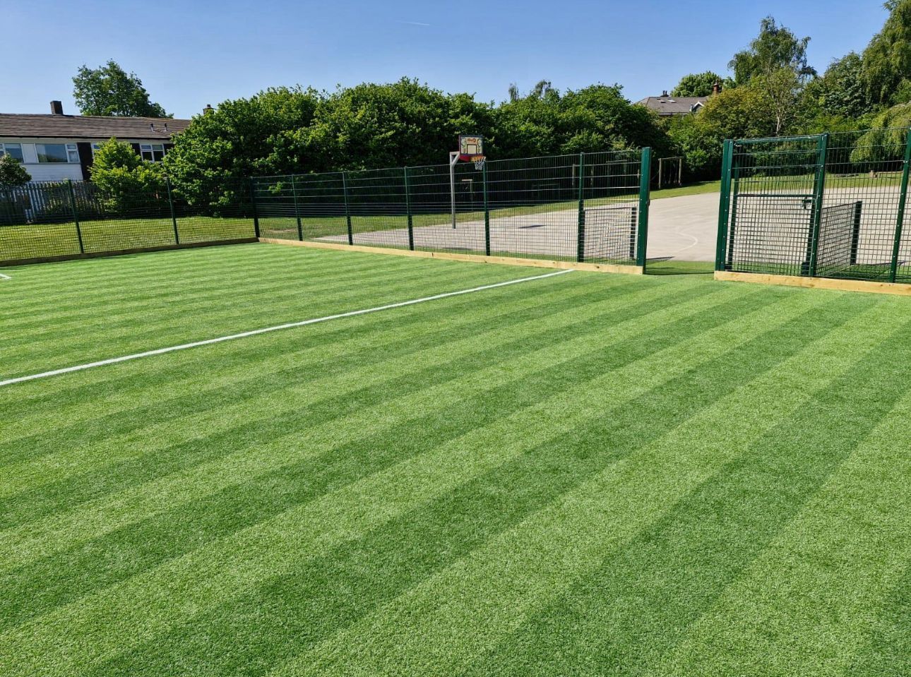 Green striped sports field beside a fenced tennis court on a sunny day