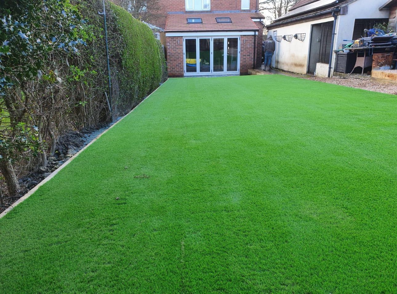 Freshly mowed green lawn leading to a brick house with glass doors and a hedge-lined side yard
