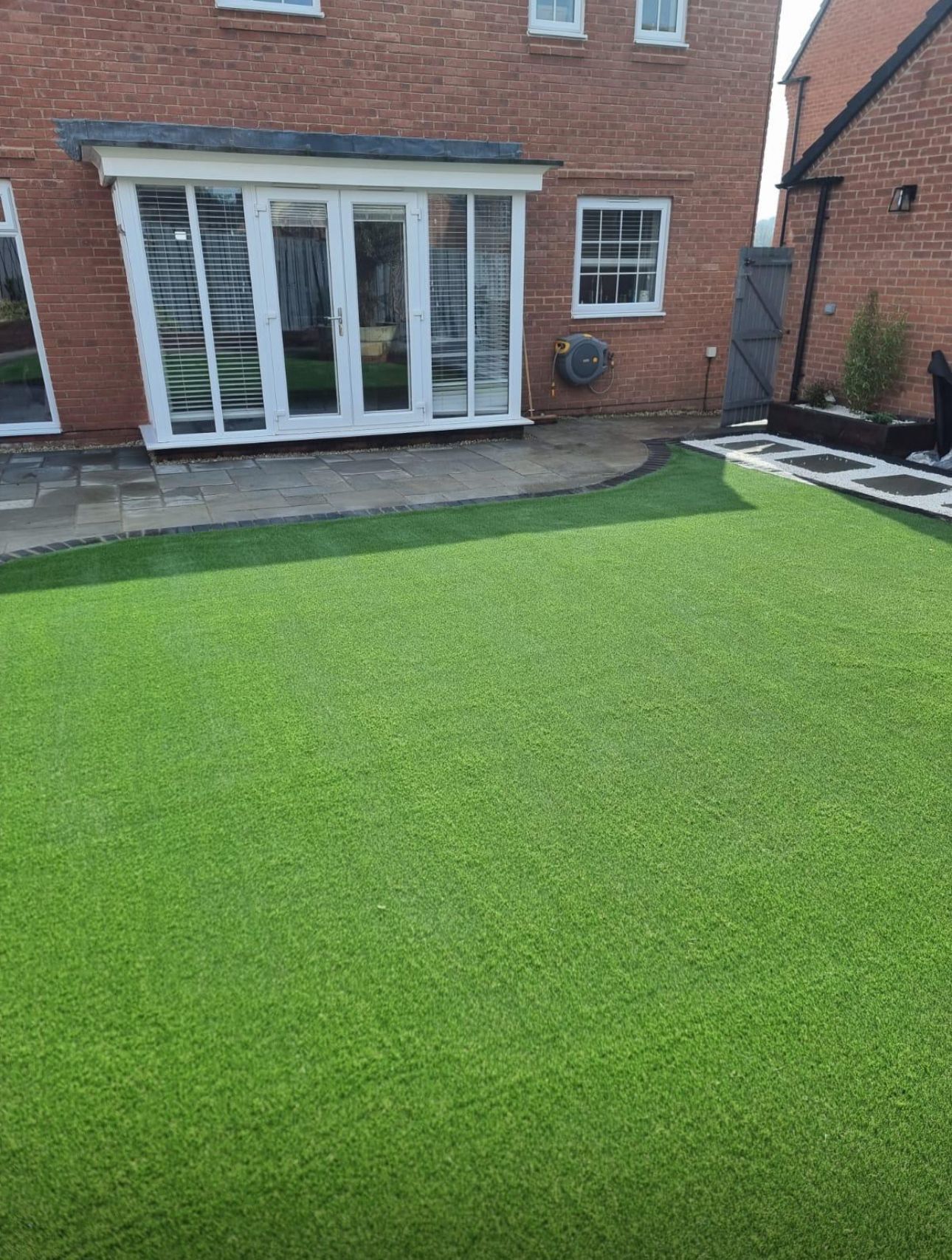 Backyard with artificial grass lawn and brick house patio doors