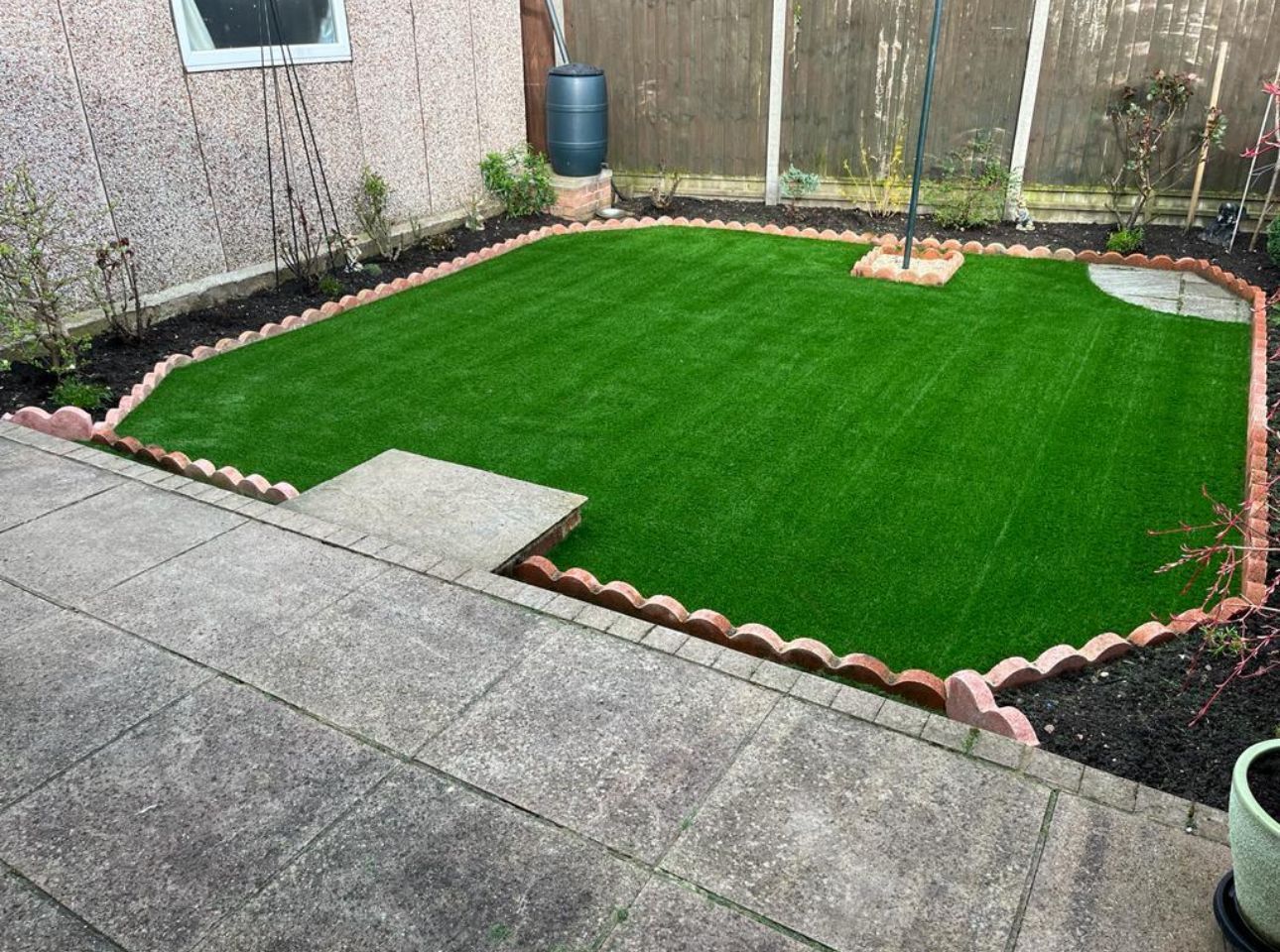 Small backyard with fresh green turf, bordered by stones and mulch, next to a concrete patio.