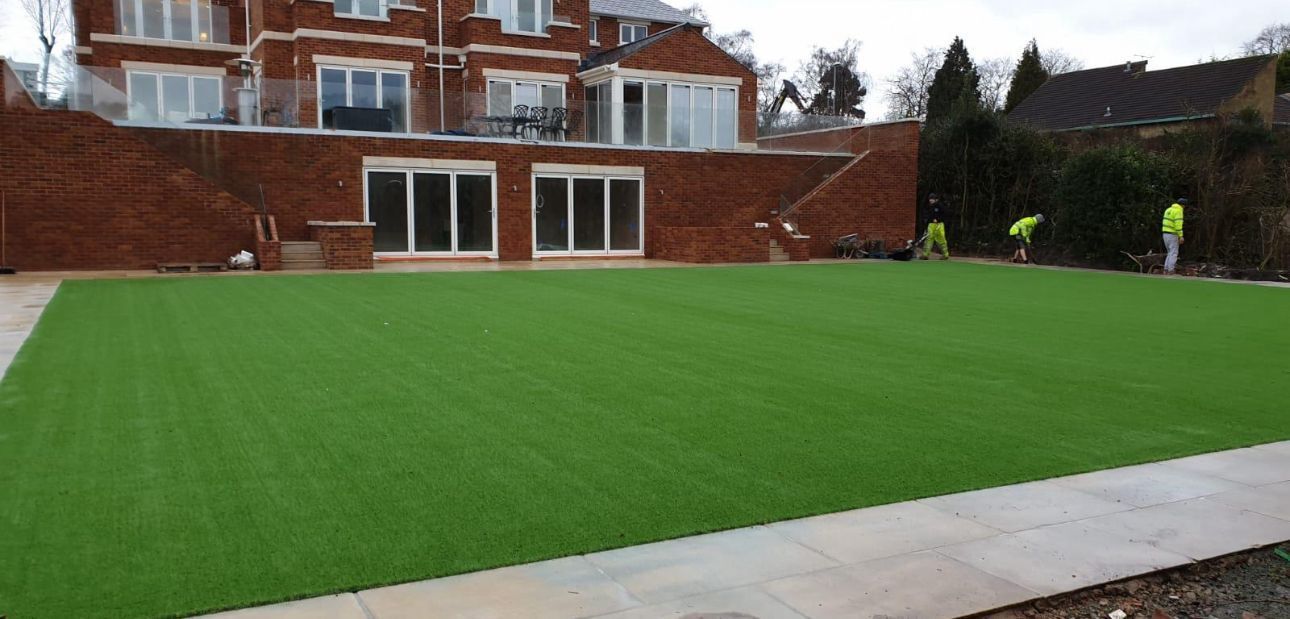 Large green lawn in a backyard with a brick house and patio in the background