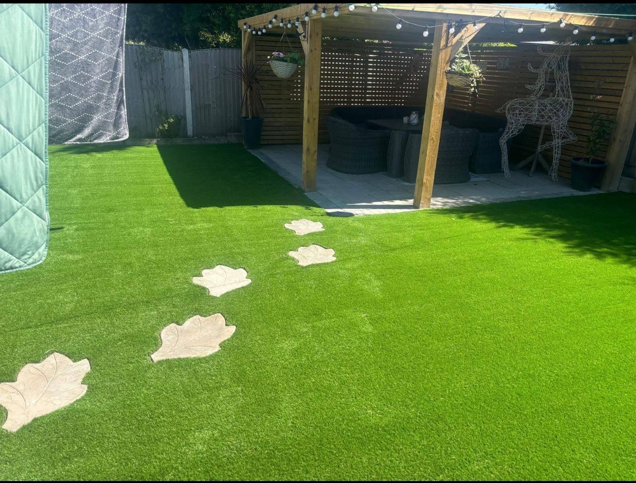 Backyard patio with green artificial grass and stepping stones leading to a shaded seating area.