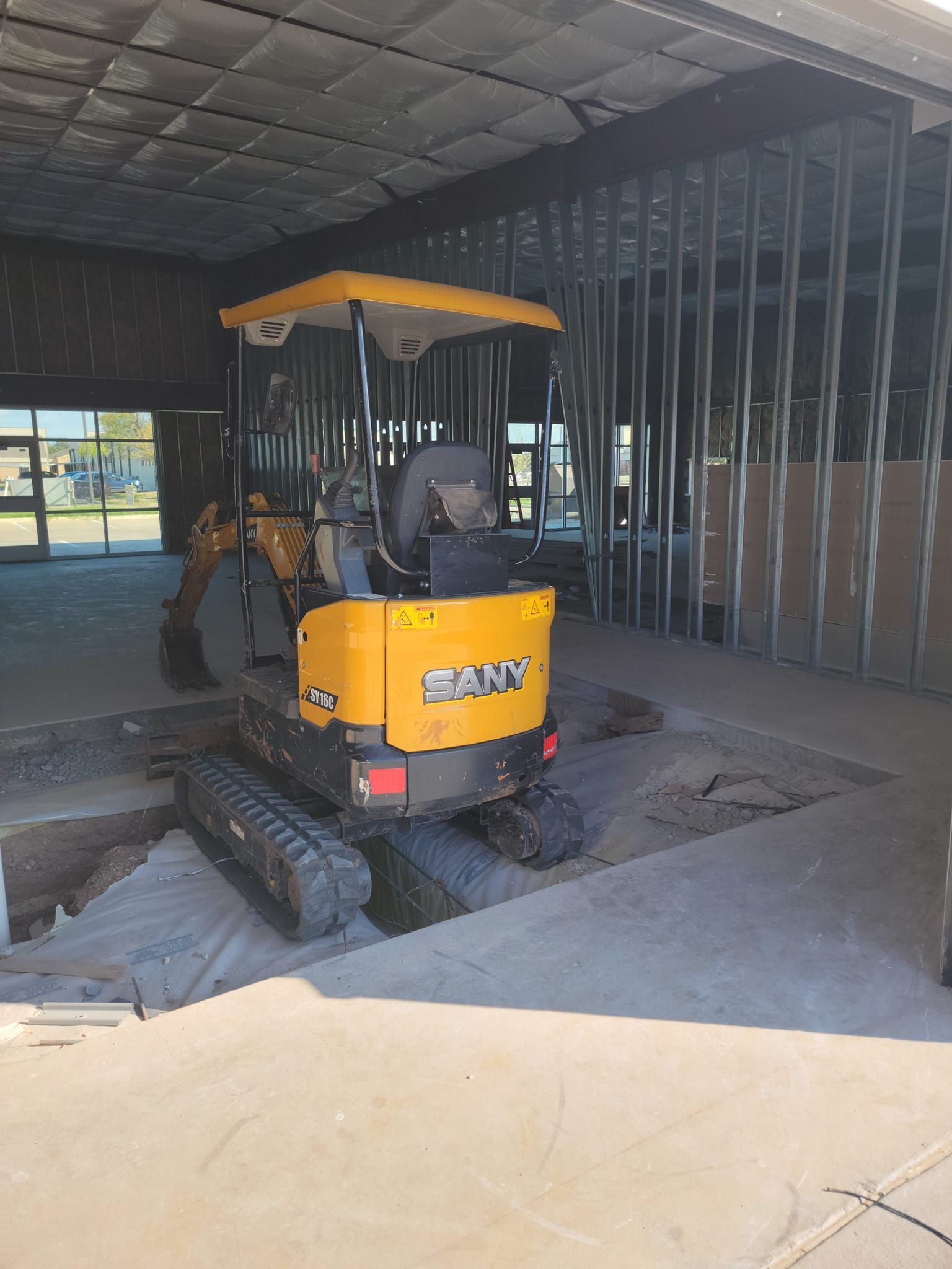 Yellow Bobcat excavator inside an unfinished building, surrounded by concrete dust and exposed framing.