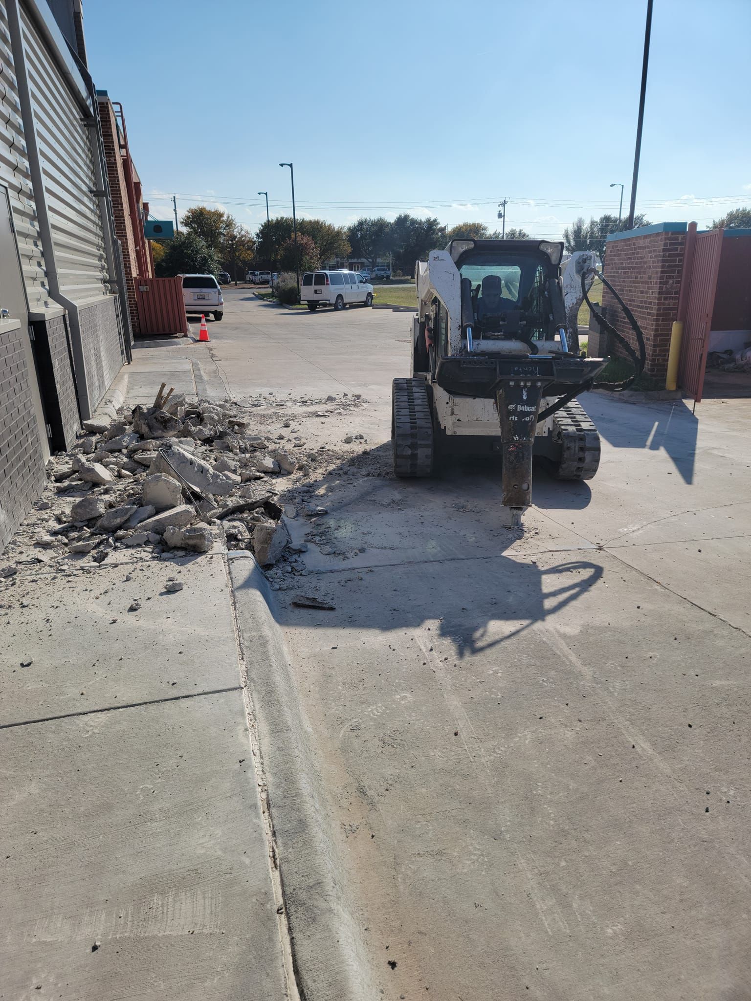 Loader clearing rubble on a concrete driveway between brick walls at an outdoor worksite.