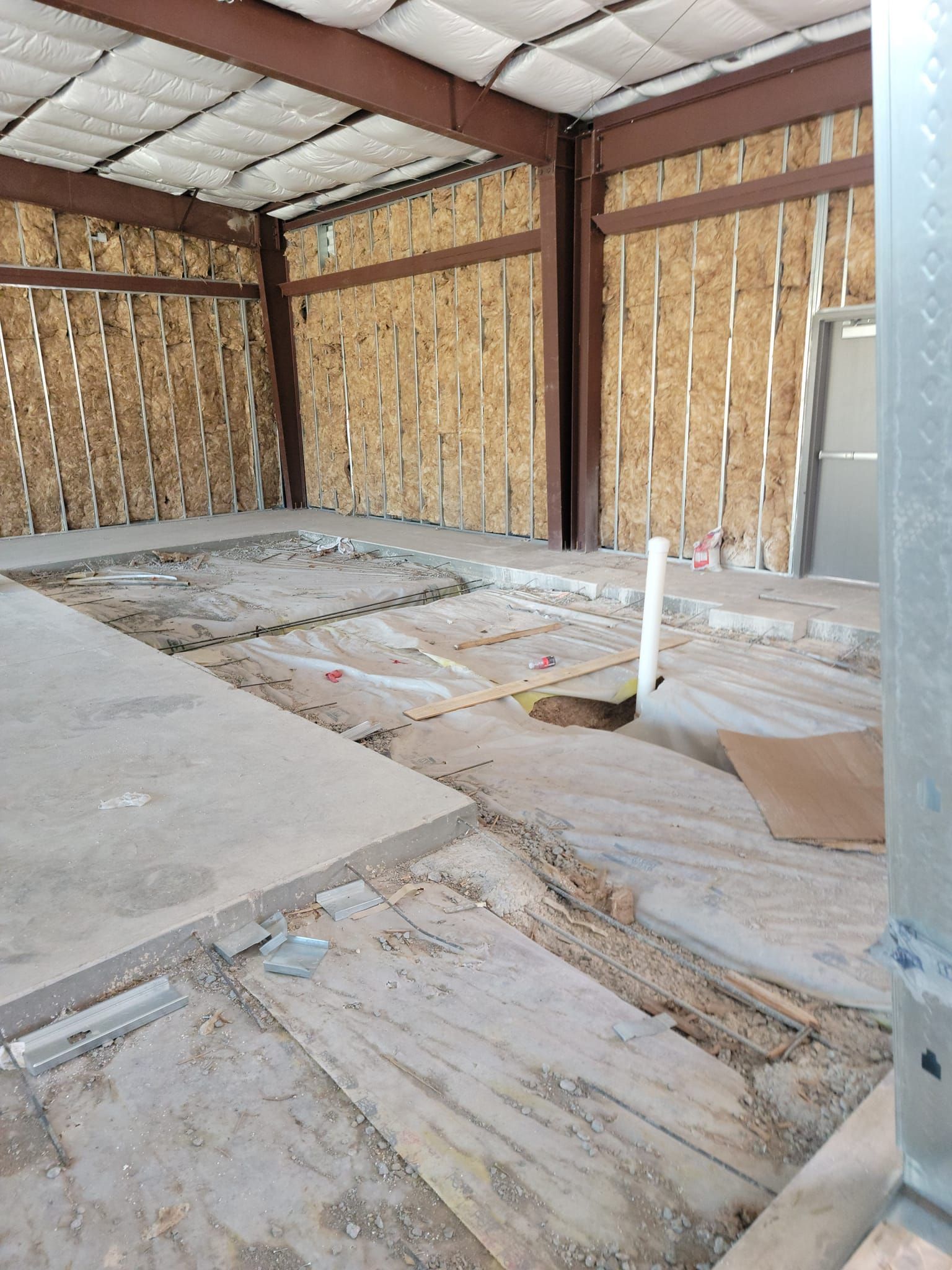 Empty unfinished room with exposed insulation, wooden walls, and a concrete floor under construction