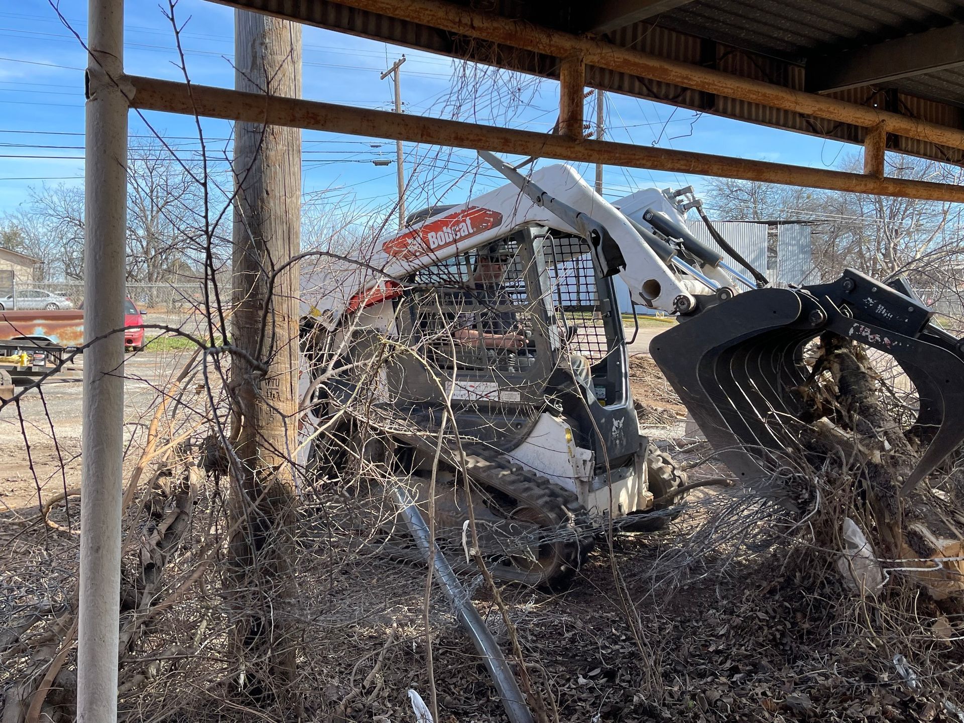 Man driving a skid steer in a muddy pen, splashing dirt under a covered structure.