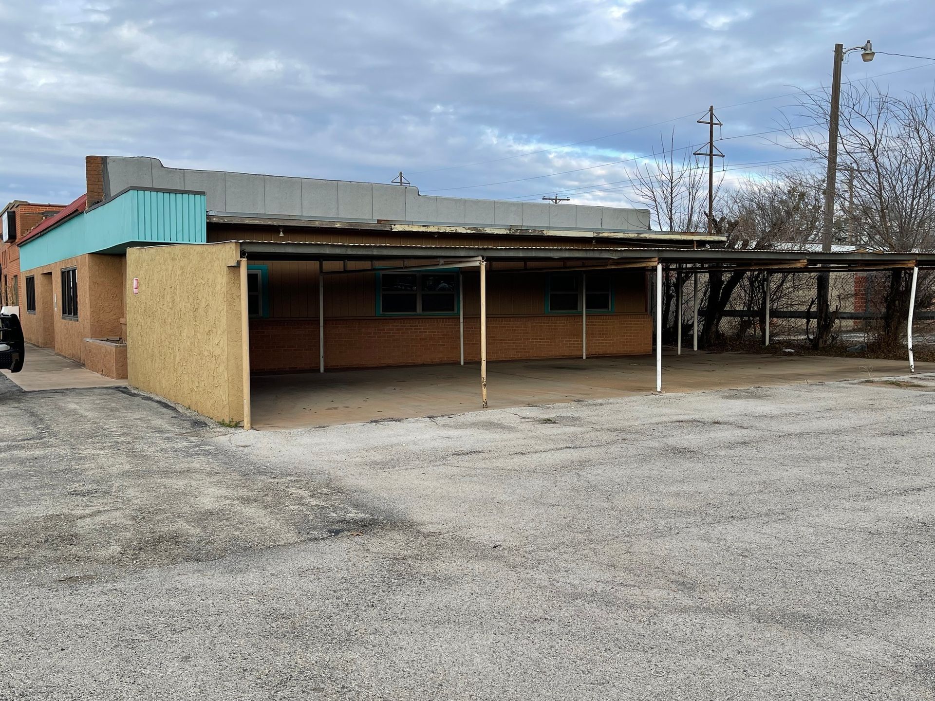 Abandoned brick building with turquoise trim and covered parking under a cloudy sky