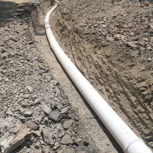 White PVC pipe laid in a dirt trench along rocky ground outdoors