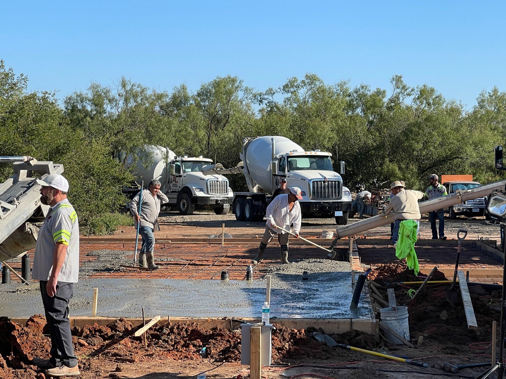 Construction workers pouring concrete at a foundation site with trucks and equipment in the background